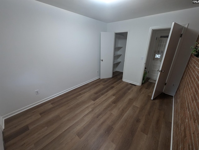 unfurnished bedroom with a spacious closet, dark wood-type flooring, brick wall, and a closet