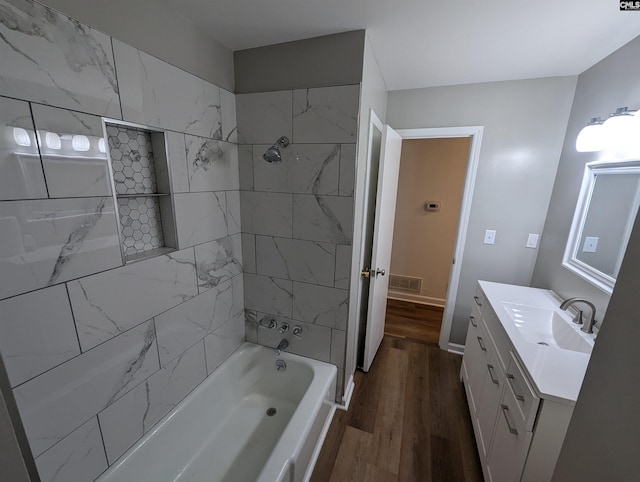 bathroom with hardwood / wood-style floors, vanity, and tiled shower / bath