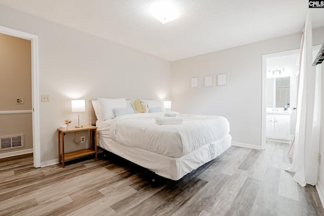 bedroom with ensuite bathroom, light hardwood / wood-style flooring, and a textured ceiling