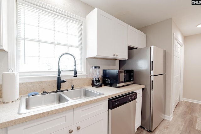 kitchen with sink, stainless steel appliances, white cabinetry, and light hardwood / wood-style flooring