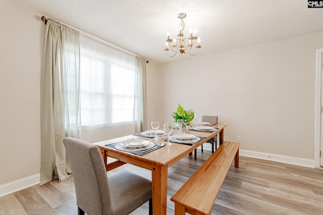 dining space featuring light wood-type flooring, a chandelier, and a textured ceiling