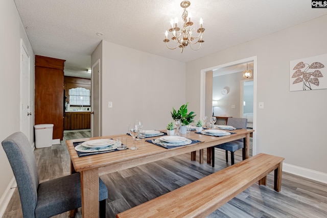 dining space featuring sink, wood-type flooring, a textured ceiling, and a notable chandelier