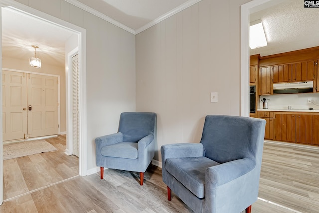 sitting room featuring light wood-type flooring, a chandelier, ornamental molding, and a textured ceiling