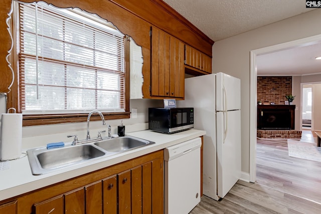 kitchen featuring sink, light wood-type flooring, a brick fireplace, white appliances, and a textured ceiling