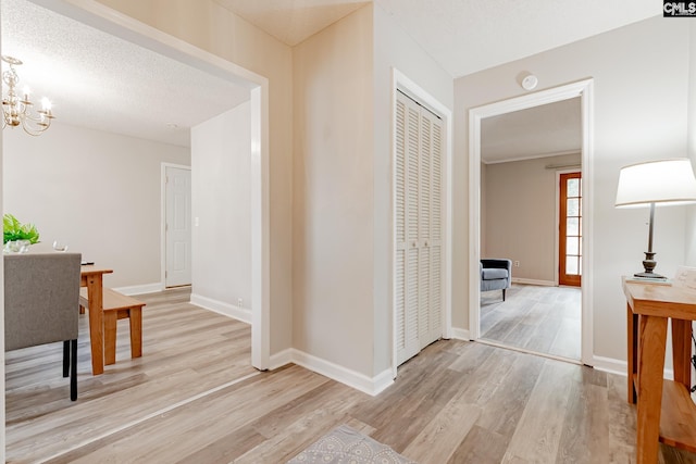 hallway with a textured ceiling, light wood-type flooring, and a chandelier