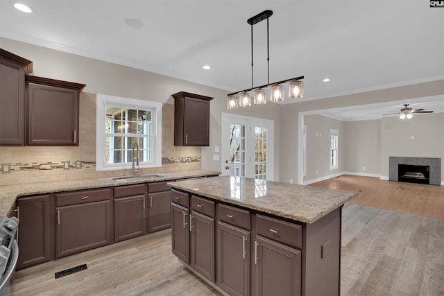 kitchen with sink, light wood-type flooring, ornamental molding, and pendant lighting