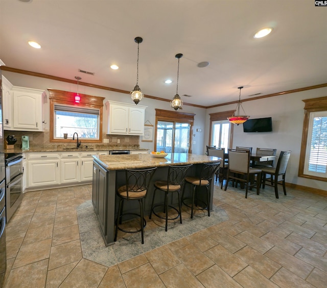 kitchen featuring a center island, backsplash, white cabinetry, and light stone counters