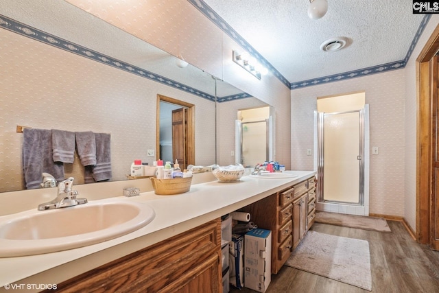 bathroom featuring hardwood / wood-style flooring, crown molding, a shower with door, vanity, and a textured ceiling