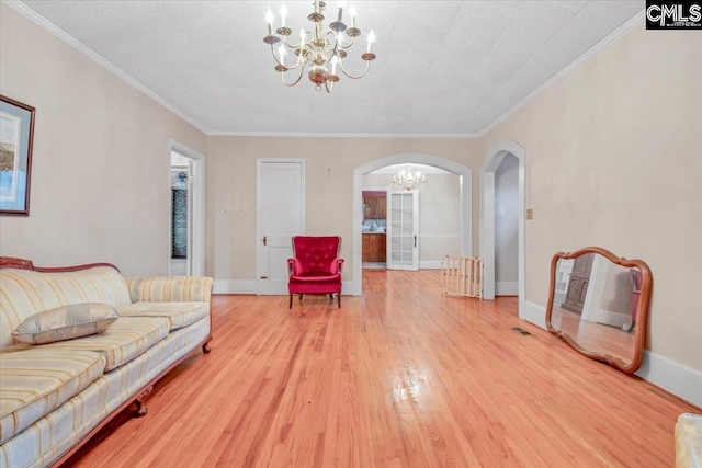 living room with a notable chandelier, light hardwood / wood-style flooring, ornamental molding, and a textured ceiling
