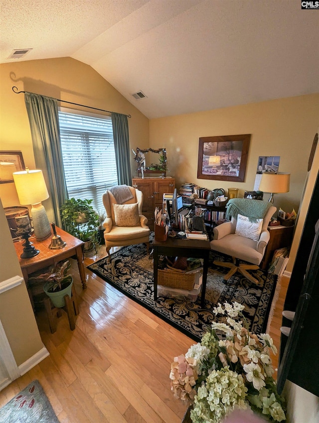 living room with hardwood / wood-style flooring, vaulted ceiling, and a textured ceiling