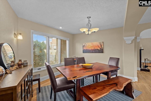 dining room featuring ornate columns, a chandelier, a textured ceiling, and light hardwood / wood-style floors