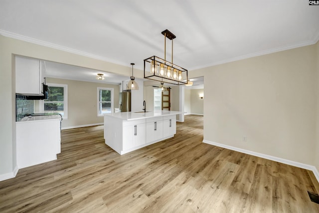 kitchen featuring white cabinetry, a center island with sink, pendant lighting, and crown molding