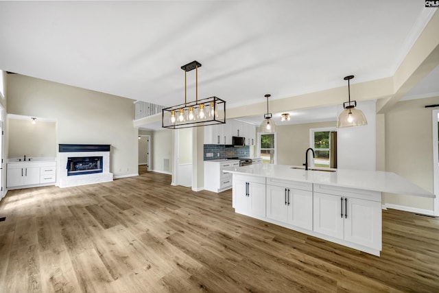 kitchen featuring sink, a kitchen island with sink, white cabinets, and pendant lighting