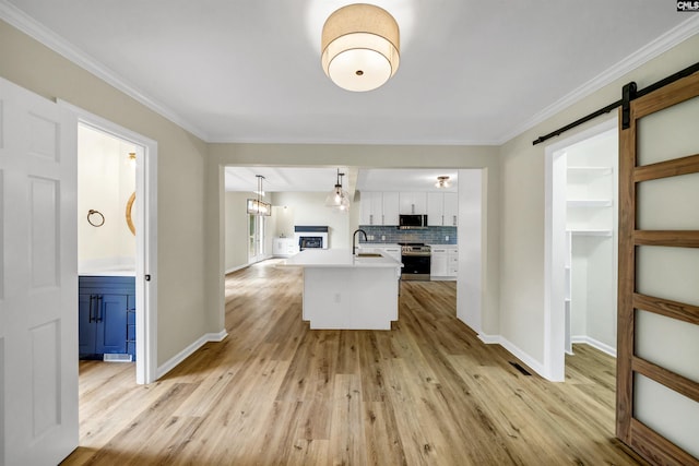 kitchen with appliances with stainless steel finishes, white cabinetry, hanging light fixtures, a barn door, and backsplash