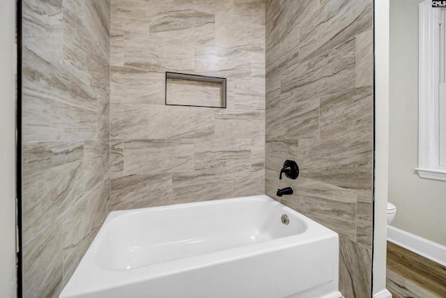 bathroom featuring wood-type flooring, toilet, and tiled shower / bath