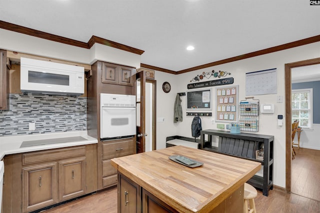 kitchen with a center island, white appliances, light hardwood / wood-style flooring, ornamental molding, and backsplash