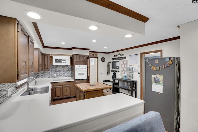 kitchen featuring sink, backsplash, kitchen peninsula, oven, and stainless steel refrigerator