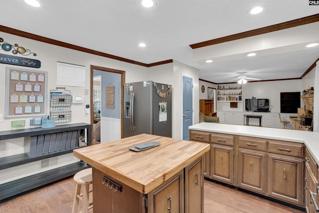 kitchen with a center island, stainless steel refrigerator with ice dispenser, butcher block counters, ornamental molding, and light hardwood / wood-style flooring