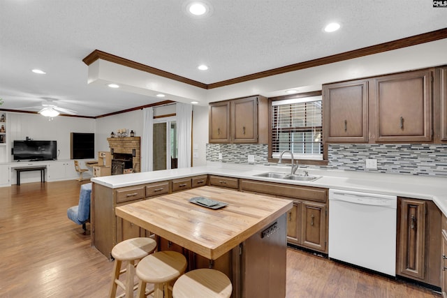 kitchen featuring butcher block counters, wood-type flooring, dishwasher, a brick fireplace, and sink