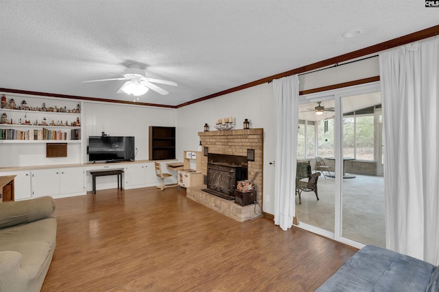 living room featuring ceiling fan, light wood-type flooring, a brick fireplace, a textured ceiling, and ornamental molding