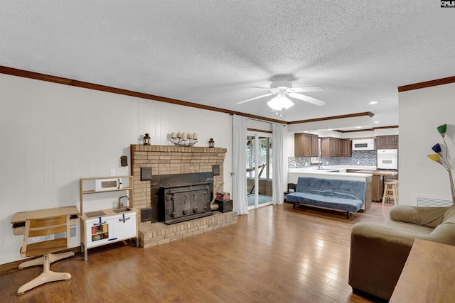 living room featuring hardwood / wood-style flooring, a textured ceiling, a brick fireplace, and ornamental molding