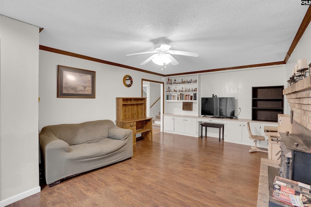 living room with a textured ceiling, hardwood / wood-style floors, built in shelves, ornamental molding, and ceiling fan