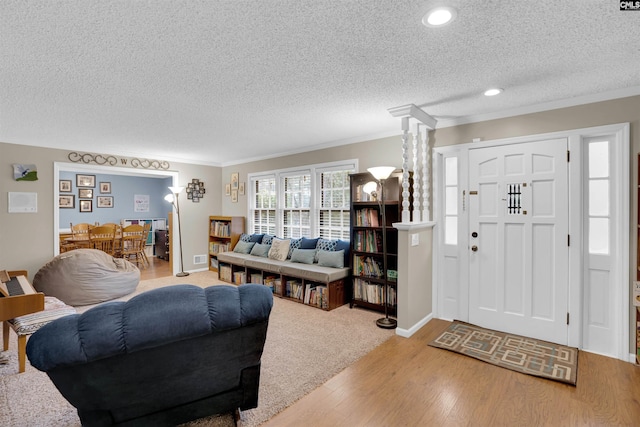 interior space featuring crown molding, hardwood / wood-style floors, a textured ceiling, and ornate columns