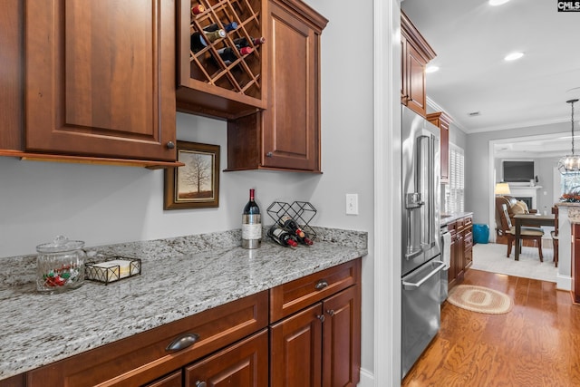 kitchen featuring high quality fridge, hardwood / wood-style floors, ornamental molding, pendant lighting, and light stone counters