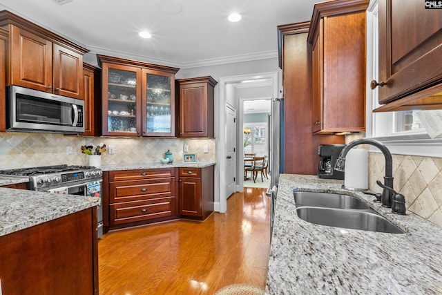 kitchen featuring light stone countertops, decorative backsplash, sink, ornamental molding, and stainless steel appliances