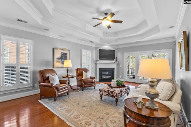 living room with ceiling fan, a raised ceiling, ornamental molding, and wood-type flooring