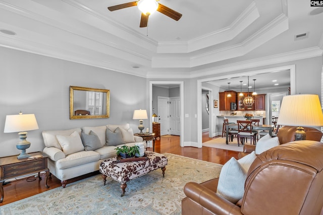 living room featuring light hardwood / wood-style flooring, a raised ceiling, ceiling fan, and ornamental molding