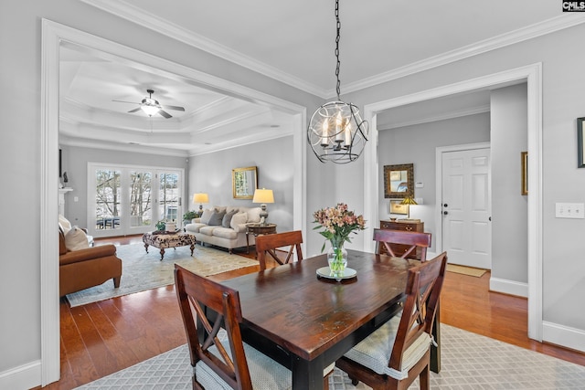 dining area featuring ceiling fan with notable chandelier, hardwood / wood-style floors, a tray ceiling, and crown molding