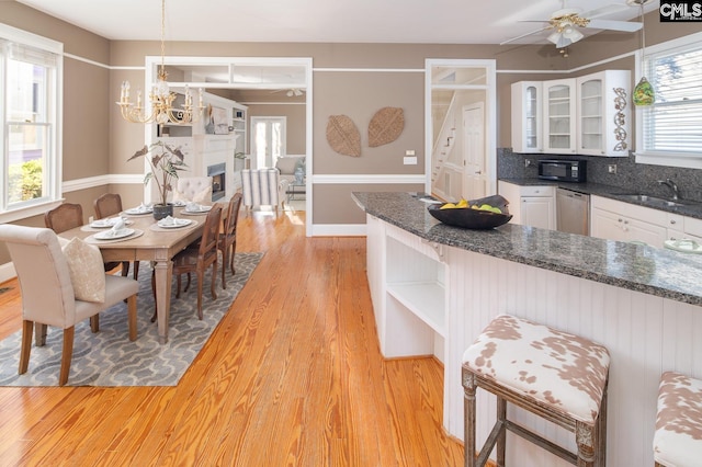 kitchen with dishwasher, white cabinetry, sink, hanging light fixtures, and light wood-type flooring