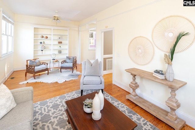 living room featuring hardwood / wood-style flooring, built in features, and ceiling fan