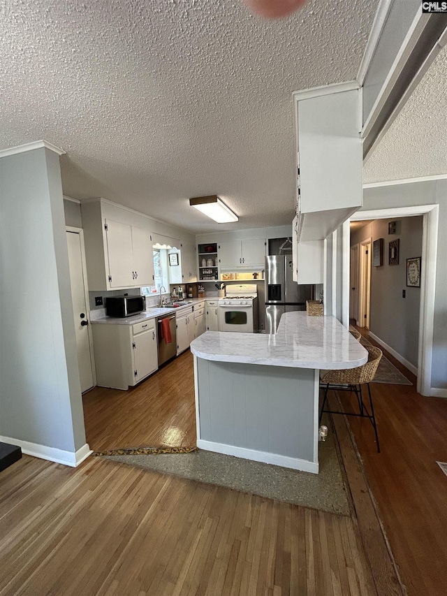 kitchen with dark hardwood / wood-style floors, white cabinetry, kitchen peninsula, stainless steel appliances, and a breakfast bar area