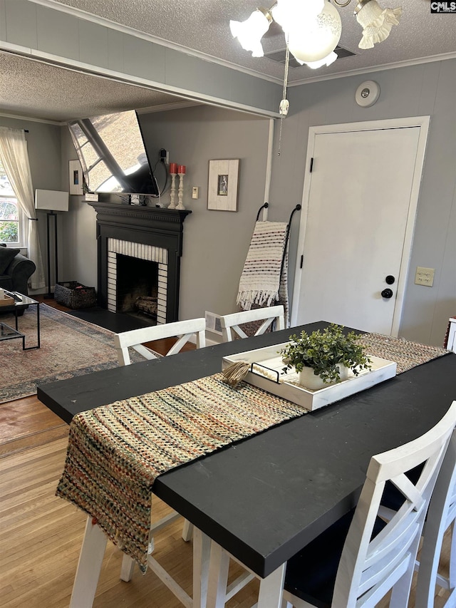 dining room with a textured ceiling, light hardwood / wood-style flooring, ornamental molding, and a fireplace