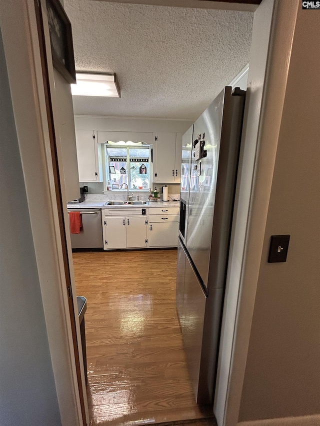 kitchen with light hardwood / wood-style flooring, sink, white cabinetry, a textured ceiling, and stainless steel appliances