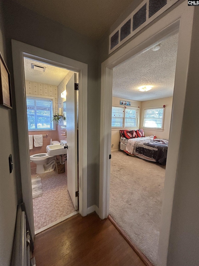 bedroom featuring ensuite bath, dark colored carpet, a textured ceiling, and multiple windows