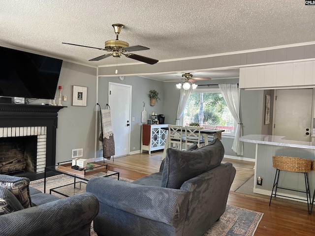 living room with a textured ceiling, dark hardwood / wood-style flooring, a fireplace, ceiling fan, and crown molding