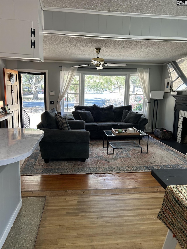 living room with a brick fireplace, a textured ceiling, hardwood / wood-style flooring, and ceiling fan