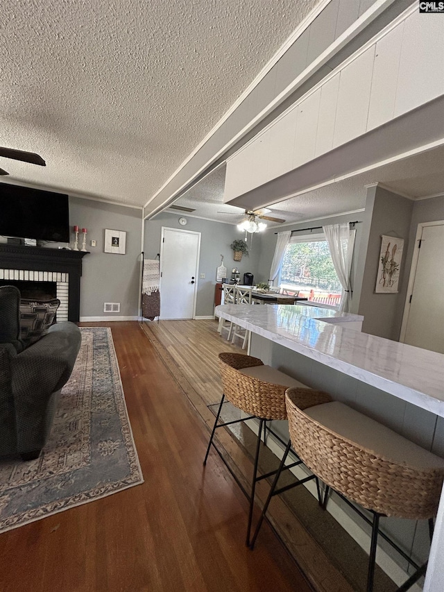 kitchen with a textured ceiling, white cabinetry, dark wood-type flooring, ceiling fan, and a breakfast bar area