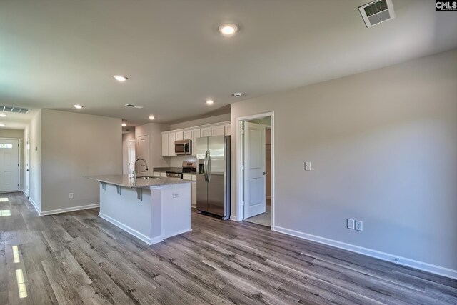 kitchen featuring white cabinetry, light stone countertops, a breakfast bar, an island with sink, and stainless steel appliances