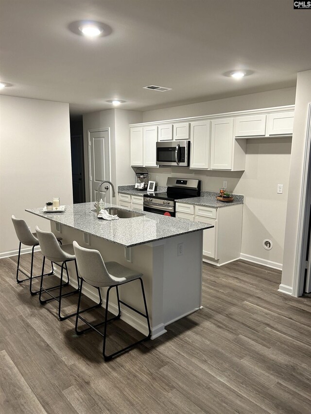 kitchen with appliances with stainless steel finishes, a kitchen island with sink, sink, white cabinets, and a breakfast bar