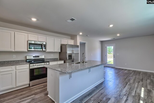 kitchen featuring a kitchen bar, appliances with stainless steel finishes, white cabinetry, a kitchen island with sink, and sink