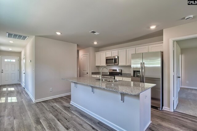 kitchen with a kitchen breakfast bar, white cabinetry, appliances with stainless steel finishes, and a center island with sink