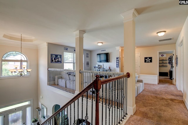 hallway featuring carpet, a chandelier, a tray ceiling, and ornate columns