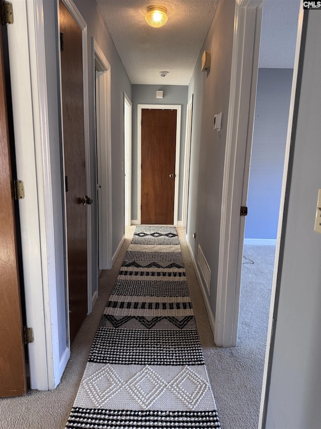 corridor with a textured ceiling and light carpet