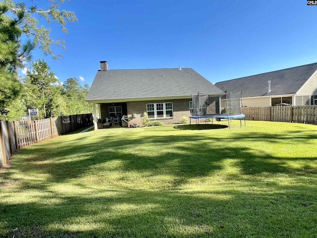 back of property featuring a trampoline and a yard