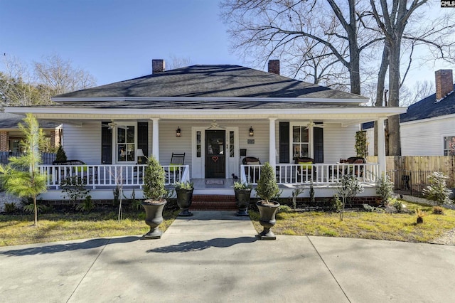 view of front of home featuring a ceiling fan, covered porch, a shingled roof, and a chimney