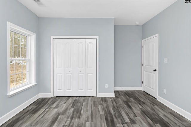 unfurnished bedroom with a closet, dark hardwood / wood-style floors, and multiple windows